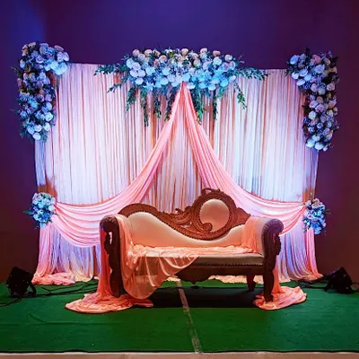 A classic engagement stage featuring an ornate sofa set against a backdrop of flowing peach drapes and lush floral arrangements, creating a romantic and timeless look.
