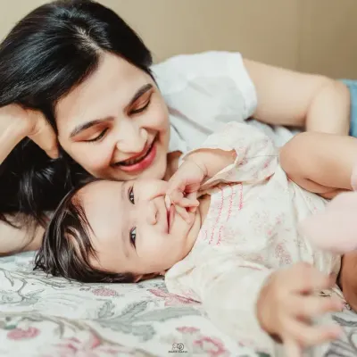 A series of candid shots from an in-home lifestyle session. A mother and her baby are playing and laughing on a bed, showcasing the natural, joyful moments I aim to capture.