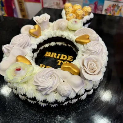A stunning ring-shaped cake for a 'Bride to Be' party. This custom design features delicate frosting, golden hearts, and is topped with Ferrero Rocher chocolates for an extra touch of luxury.
