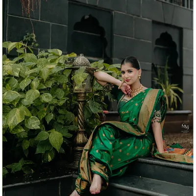 A stunning portrait of a Maharashtrian bride in a rich green Paithani saree. Her graceful pose on the steps, surrounded by greenery, highlights her timeless elegance.