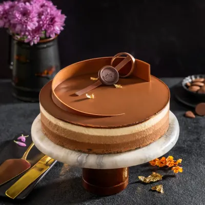 A multi-layered chocolate mousse cake with a glossy finish and an elegant chocolate swirl, presented on a marble cake stand for a sophisticated dessert shot.