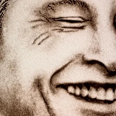 Can you guess who this is? A close-up detail of a sand portrait capturing the iconic smile of a visionary. The texture of the sand adds a unique depth to the expression.