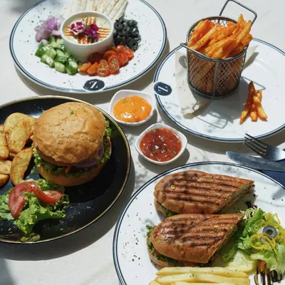 My lunch spread is designed for sharing and savoring. It features a juicy burger with potato wedges, a grilled panini, a fresh hummus platter, and a basket of crispy fries.