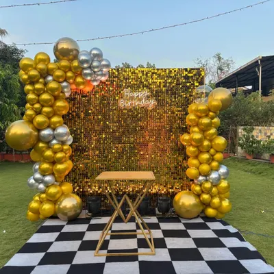 For a stunning outdoor 40th birthday, we set up a glamorous gold shimmer wall with a 'Happy Birthday' neon sign. The backdrop is framed by organic balloon columns in gold and silver, set on a checkered floor for a chic and modern party vibe.