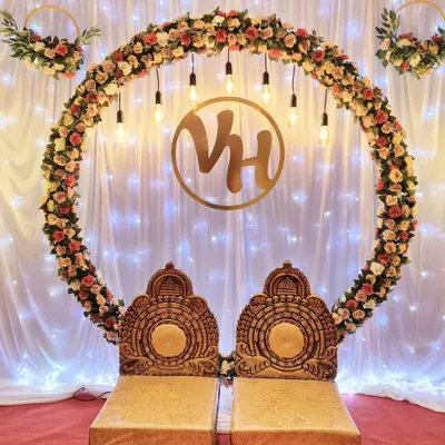 A stunning engagement stage featuring a large ring made of artificial roses, illuminated by hanging Edison bulbs. A custom gold monogram and traditional seating complete this classic and elegant look.