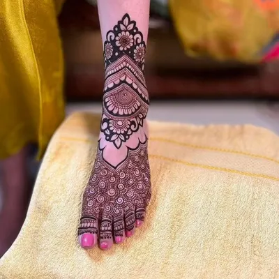 A close-up of a detailed foot mehandi design. This pattern covers the top of the foot with a beautiful floral and paisley pattern, ending in delicate swirls on the toes.