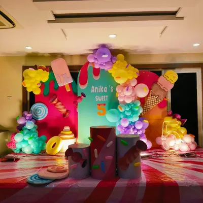 A super sweet ice cream and candy theme for a 5th birthday. The colorful setup includes cutouts of ice cream cones and popsicles, themed plinths, and a light-up number '5', creating a fun Candyland atmosphere.