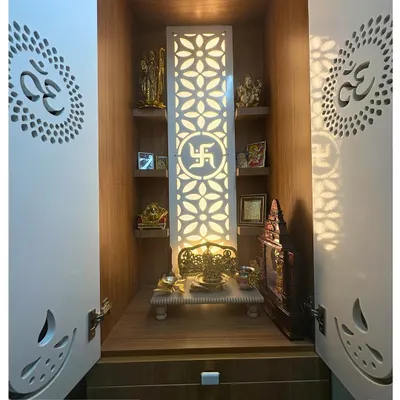 A beautiful pooja unit with backlit jaali doors featuring the 'Om' symbol. The interior has ample shelving for idols and drawers for storage, creating a serene and organized sacred space.