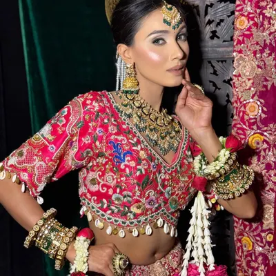 This is a classic Indian bridal look, featuring a sharp, winged eyeliner and a glowing, sculpted base. The makeup is designed to complement the heavy embroidery of the lehenga and the traditional polki jewellery.