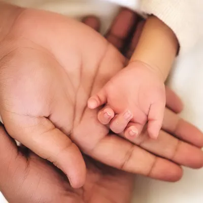 A macro shot of a newborn's tiny hand resting in their parent's palm. This simple, powerful image shows the scale of how small and precious they are.
