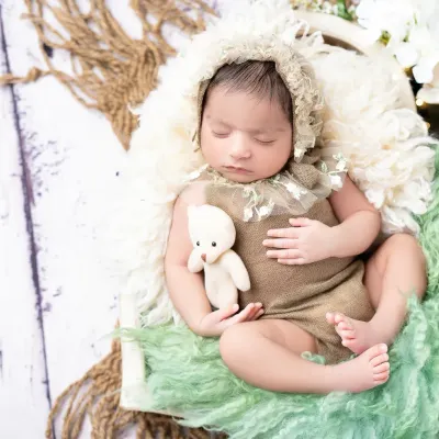 A peaceful newborn rests with a tiny teddy bear, styled with soft, earthy tones and textures. This classic newborn pose highlights the baby's delicate features in a safe and comfortable setting.