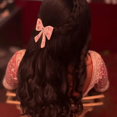 A romantic half-up, half-down hairstyle with soft curls. The look is finished with a delicate, sparkling bow, making it perfect for a reception or engagement party.
