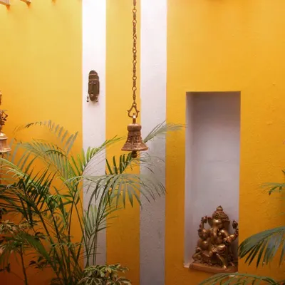 A vibrant garden wall painted in a cheerful yellow, adorned with traditional brass bells and a Ganesha idol. This small corner becomes a space of peace and positive energy, blending spiritual elements with bold color.