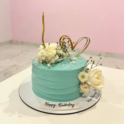 A slice of floral heaven. This elegant birthday cake has a textured teal buttercream finish and is decorated with fresh white flowers, baby's breath, and a delicate gold heart topper.