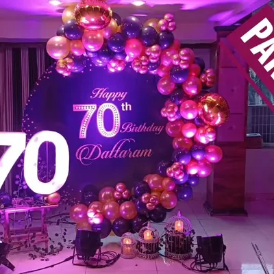 A grand 70th birthday celebration for Dattaram, featuring a deep purple and gold balloon arch, a custom backdrop, and large light-up marquee numbers.