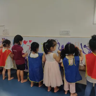 This is what a collaborative art session looks like. A group of children stands side-by-side, each contributing to a large-scale mural, learning to share space and ideas while exploring colors and shapes.
