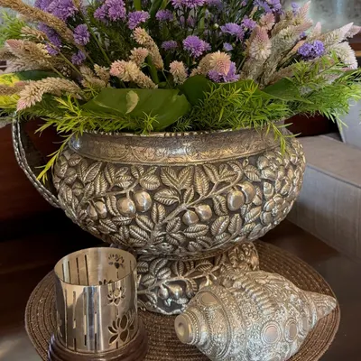 Luxury is in the details. This exquisite silver decorative bowl, intricately carved with floral patterns, is filled with a beautiful arrangement of purple and white flowers, creating a truly opulent centerpiece.