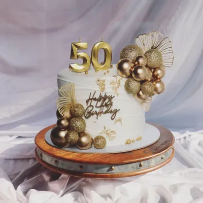 Celebrating a golden milestone. This 50th birthday cake is pure glamour, featuring gold balloon clusters, gold leaf, and a bold number '50' topper.