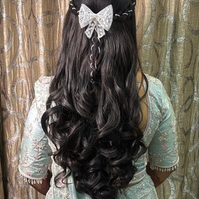 A fairytale hairstyle for a bride. This look features long, flowing curls with a delicate white bow accessory, perfect for a reception or engagement.