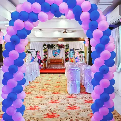 A grand balloon arch in pink and blue creates a welcoming entrance for guests at a baby shower. This view shows how the entrance decor sets the tone for the main event stage in the background.