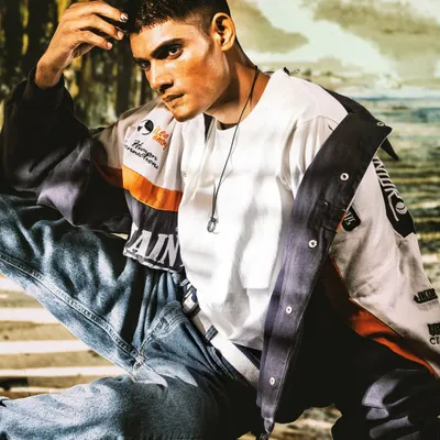 A relaxed yet stylish portrait. The projected beachside background and warm lighting create a casual, lifestyle feel that complements the modern, layered outfit.