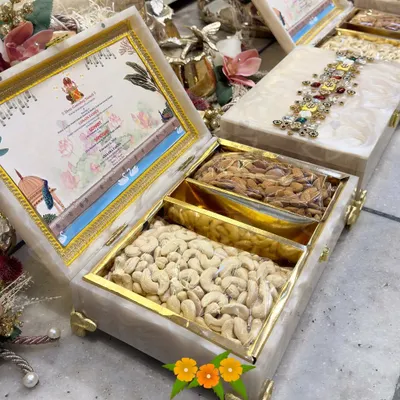 Wedding favors that make a statement. This is a luxury invitation box made of resin, featuring a custom-designed card and compartments for premium cashews and almonds. The top is adorned with intricate jeweled work.