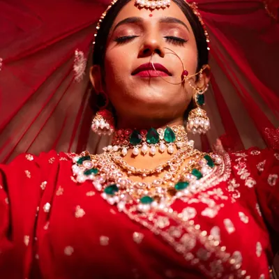 A stunning bridal portrait where the bride is enveloped in her red veil. This shot is all about capturing a moment of serene beauty and the richness of the bridal attire.