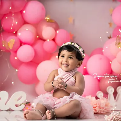 A picture of pure happiness for her first birthday. We create stunning setups with balloon arches and custom props to make your baby's "One" year milestone truly special.