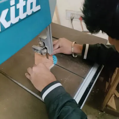 A student using the bandsaw to make a precise curved cut. This is part of a workshop where interior design students learn to use tools to build their own designs.