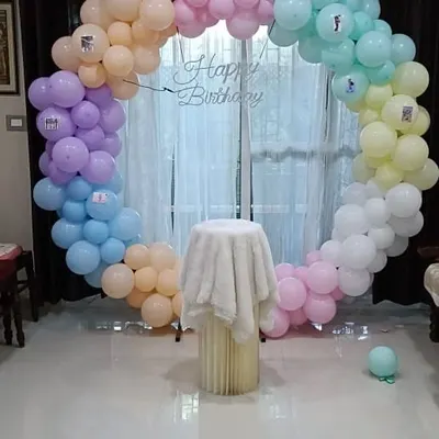 A circular balloon arch created with smaller balloons in pastel shades of pink, blue, purple, and peach. This setup was designed as a photo backdrop for a birthday party, complete with a "Happy Birthday" sign.