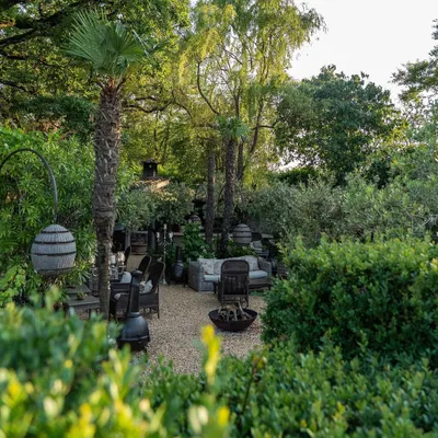 A rustic yet sophisticated outdoor lounge area nestled within a lush garden. We used gravel flooring, comfortable wicker furniture, and a central fire bowl to create an inviting space for gathering with friends and family.