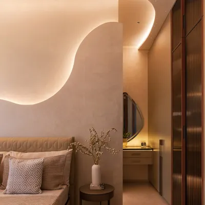 This bedroom is a perfect example of soft, sculptural minimalism. The curved, illuminated wall detail creates a gentle, flowing backdrop for the bed, while the layered neutral bedding and fluted wardrobe doors add tactile warmth.