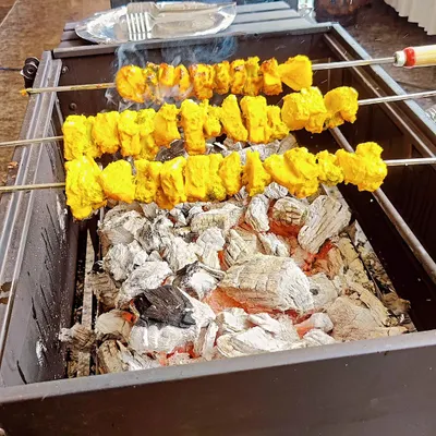 Skewers of marinated paneer and pineapple tikka sizzling over glowing charcoal embers. This close-up shows the delicious char and color we achieve at our live tandoor and barbecue station, a highlight for any event.