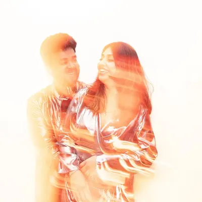 An abstract portrait created with motion blur and warm, orange light flares. The couple is captured in an embrace, their forms blending together in a swirl of color and energy, giving a dreamy, artistic feel.
