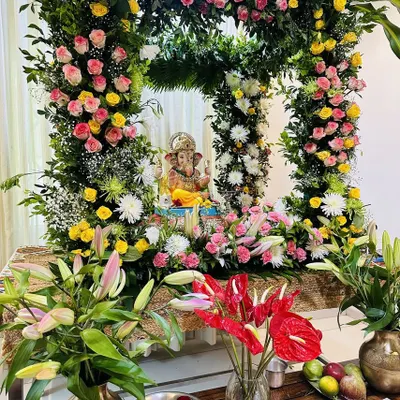 A beautiful and dense floral frame for a home Ganpati celebration. This arrangement is rich with pink and yellow roses, lilies, and anthuriums, creating a full and festive look that surrounds the idol in natural beauty.