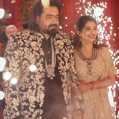 A grand entrance for a lifetime of smiles. The bride glows in a golden lehenga, perfectly complemented by the groom's black sherwani featuring intricate white floral embroidery.