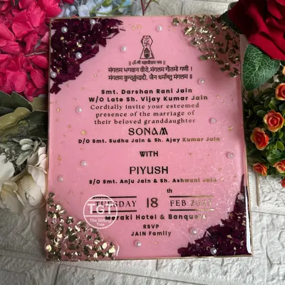 An 8x10 inch resin wedding invitation with a glittery baby pink base. The design features preserved rose petals and stones on diagonal corners, with pearls for an elegant touch.
