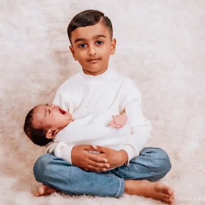 A heartwarming portrait of a big brother proudly holding his newborn sibling. The genuine smile on his face shows the love and excitement of his new role.