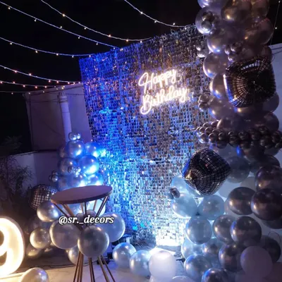 A glamorous rooftop party for a 29th birthday, featuring a silver shimmer wall, a balloon garland, fairy lights, and a glowing neon sign.