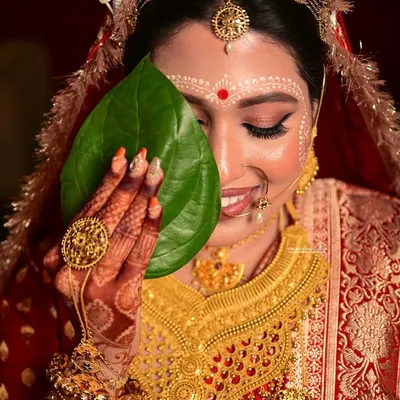 A classic Shubho Drishti moment. The bride's shy smile behind the betel leaves is a cherished part of the Bengali wedding ceremony, and I aim to capture its innocence and beauty.