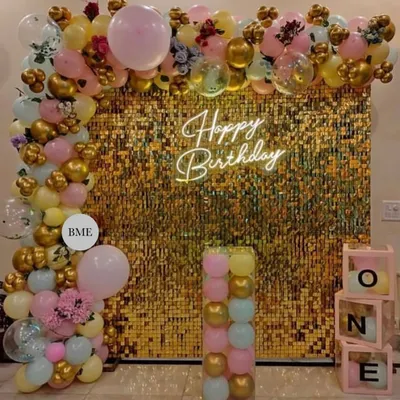 A glamorous birthday decoration with a golden sequin wall. The setup is framed by a pastel balloon arch and includes 'ONE' display boxes, perfect for a stylish first birthday party.