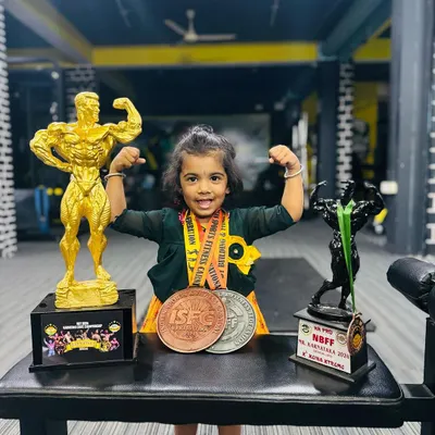 My daughter posing with my Mr. Karnataka 2024 trophies. I want every kid at my camp to feel this same pride and confidence in their own achievements, big or small.