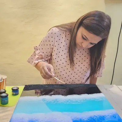 Creating a black sand beach effect. Here, a student is carefully adding details to an ocean art piece, learning how to create depth and texture with different resin pouring techniques.