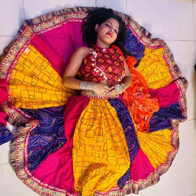 An artistic top-down shot of a model lying down, with her colorful Garba lehenga spread out in a perfect circle. This showcases the vibrant colors and wide flare of my chaniya choli collection.