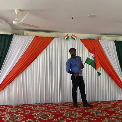 A stage setup for an Independence Day celebration, featuring a backdrop with the tricolor drapes and Indian flags.