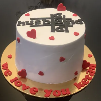 A special cake celebrating a husband and dad. This bento cake features a unique "husband" and "dad" crossword design on top, surrounded by red hearts and a loving message around the base.