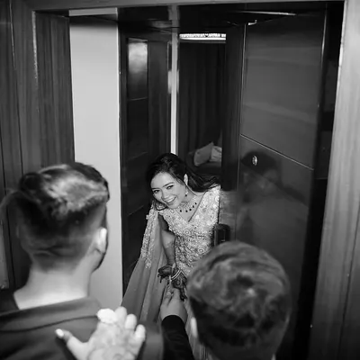 A candid moment captured in monochrome. The bride peeks out from a doorway with a joyful laugh, and the black and white treatment emphasizes the raw emotion and happiness of the moment.