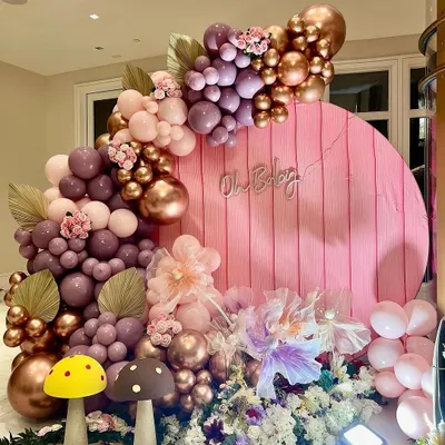 A wide view of the whimsical woodland baby shower setup. The round pink backdrop with the "Oh Baby" sign is framed by a lush balloon garland in shades of mauve and rose gold, with mushroom props adding a touch of fairytale magic.