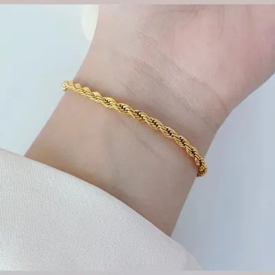 A classic and sturdy gold-toned rope bracelet shown on the wrist. This timeless piece is made with color-stable materials for long-lasting wear.