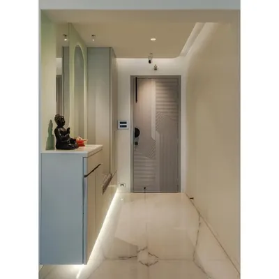 This entryway features a floating console in a sophisticated grey matte laminate, providing storage right by the door. The design is enhanced by a pastel green accent wall, an arched mirror, and cove lighting for a warm and inviting welcome.